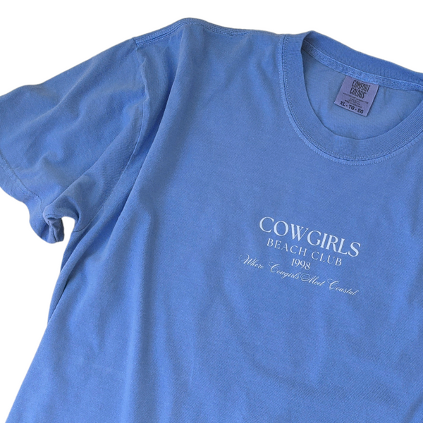 This Cowgirls Coastal Beach Club Graphic Tee is the perfect blend of western charm and summer style! This blue tee features a minimal front text and a fun beachy western graphic on the back—designed for trend-lovers and sunshine-chasers. Great for pairing with denim shorts, cowboy boots, or a trucker hat for the full cowgirl vibe. For that oversized, slouchy look, size up!