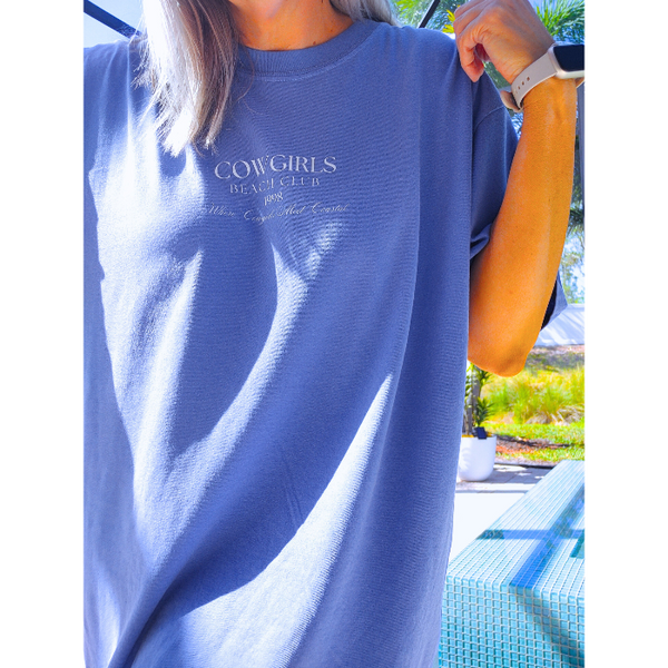 This Cowgirls Coastal Beach Club Graphic Tee is the perfect blend of western charm and summer style! This blue tee features a minimal front text and a fun beachy western graphic on the back—designed for trend-lovers and sunshine-chasers. Great for pairing with denim shorts, cowboy boots, or a trucker hat for the full cowgirl vibe. For that oversized, slouchy look, size up!