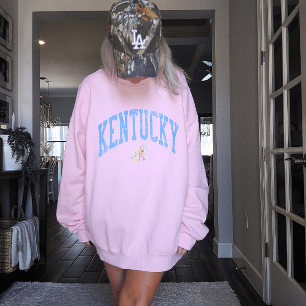 Stay cozy and stylish with our Kentucky sweatshirt, available in light pink and white! Featuring a cute coquette preppy horse with a bow, this distressed design is perfect for any horse lover or cowgirl. Ideal for a Kentucky derby outfit or as a gift, size up for an oversized fit. Order now and show off your love for all things western!