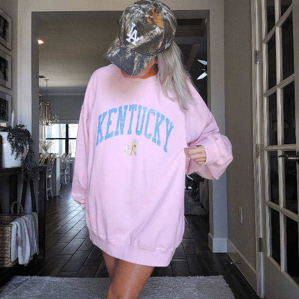 Stay cozy and stylish with our Kentucky sweatshirt, available in light pink and white! Featuring a cute coquette preppy horse with a bow, this distressed design is perfect for any horse lover or cowgirl. Ideal for a Kentucky derby outfit or as a gift, size up for an oversized fit. Order now and show off your love for all things western!