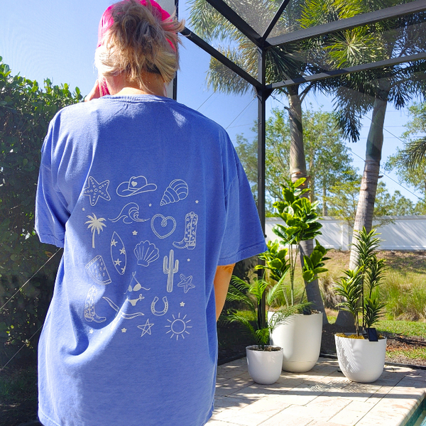 This Cowgirls Coastal Beach Club Graphic Tee is the perfect blend of western charm and summer style! This blue tee features a minimal front text and a fun beachy western graphic on the back—designed for trend-lovers and sunshine-chasers. Great for pairing with denim shorts, cowboy boots, or a trucker hat for the full cowgirl vibe. For that oversized, slouchy look, size up!