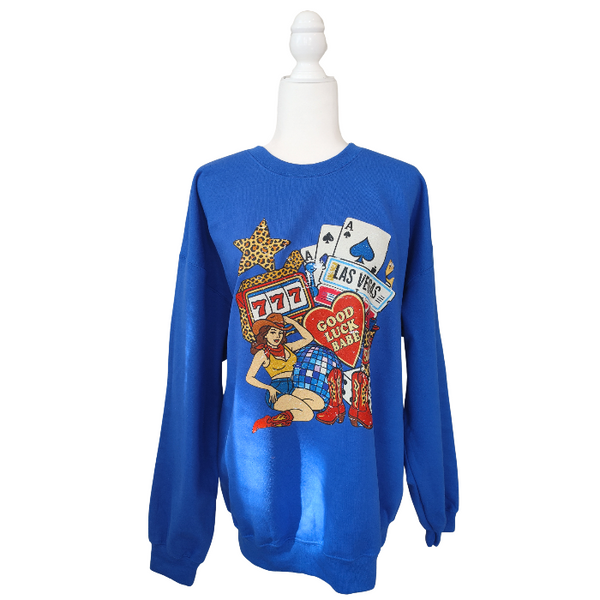 Turn up the lucky vibes with this bold and retro-inspired Las Vegas graphic sweatshirt. Designed in a vibrant royal blue, this cozy pullover features the ultimate “Good Luck Babe” casino theme—complete with slot machine sevens, cowgirl art, leopard-print star, poker cards, and classic Western boots. It’s the perfect mix of vintage charm, playful style, and standout color.