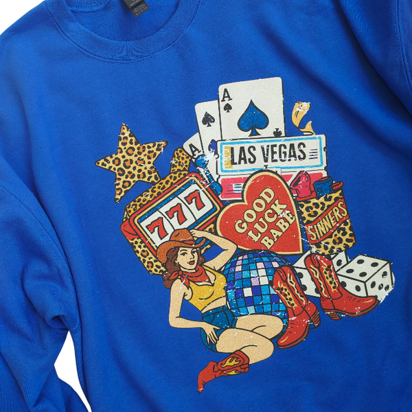 Turn up the lucky vibes with this bold and retro-inspired Las Vegas graphic sweatshirt. Designed in a vibrant royal blue, this cozy pullover features the ultimate “Good Luck Babe” casino theme—complete with slot machine sevens, cowgirl art, leopard-print star, poker cards, and classic Western boots. It’s the perfect mix of vintage charm, playful style, and standout color.