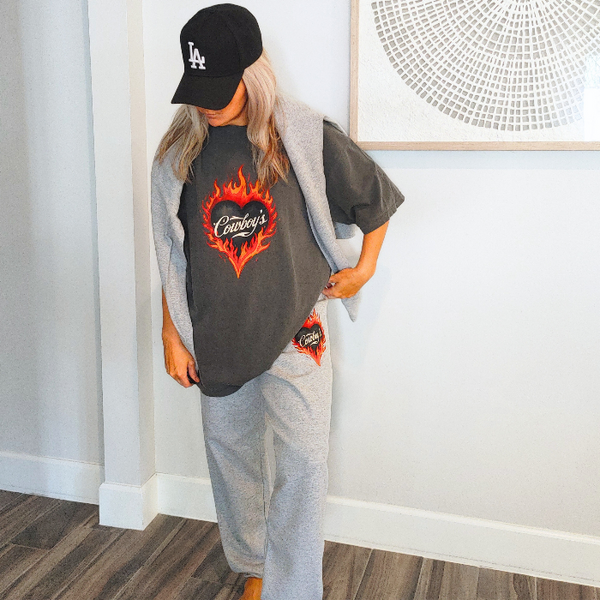 Bring bold western energy to your everyday wardrobe with these Cowboys flame sweatpants. Featuring a striking flaming heart “Cowboys” graphic, these gray jogger-style sweatpants are designed for laid-back comfort with a statement edge. They have an oversized fit for that relaxed, effortlessly look. They feature a drawstring elastic waistband and elastic cuffs for all-day comfort and an easy fit.