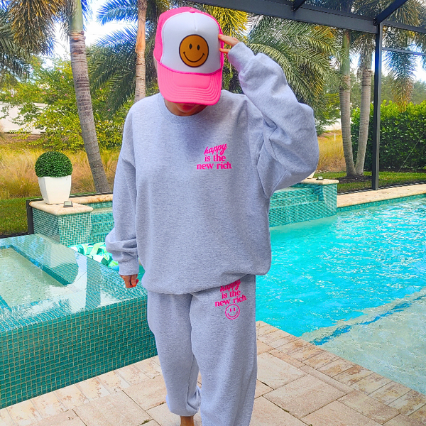 Bring all the good vibes with this cozy “Happy Is the New Rich” smiley face sweatshirt. Featuring a bold neon-pink front chest quote and an oversized happy face graphic on the back, this crewneck is designed to make every outfit feel a little brighter. This soft, comfy unisex crewneck makes the perfect gift and for everyday wear, this is your new go-to layer for errands, lounging, weekend adventures, and everything in between. Pair it with our matching sweatpants (sold separately) for the full set. 