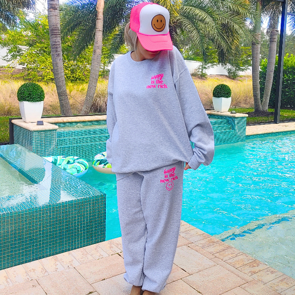 Bring all the happy vibes with these trendy “Happy Is the New Rich” smiley face sweatpants. Designed in a classic ash gray and featuring the saying “Happy Is the New Rich” along with a bold neon-pink happy face graphic, these joggers are the perfect mix of comfy, cute, and on-trend. With a relaxed, oversized fit and an elastic waistband, they’re your new everyday go-to. They pair perfectly with our matching sweatshirt (sold separately) to complete the loungewear set — and they also make the perfect gift!