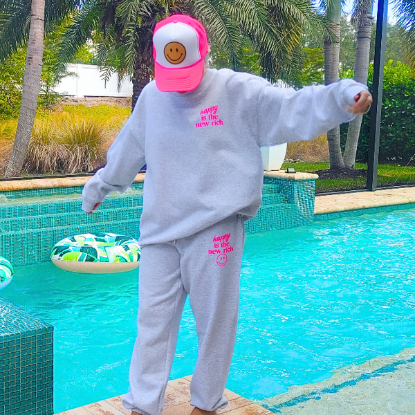 Bring all the happy vibes with these trendy “Happy Is the New Rich” smiley face sweatpants. Designed in a classic ash gray and featuring the saying “Happy Is the New Rich” along with a bold neon-pink happy face graphic, these joggers are the perfect mix of comfy, cute, and on-trend. With a relaxed, oversized fit and an elastic waistband, they’re your new everyday go-to. They pair perfectly with our matching sweatshirt (sold separately) to complete the loungewear set — and they also make the perfect gift!