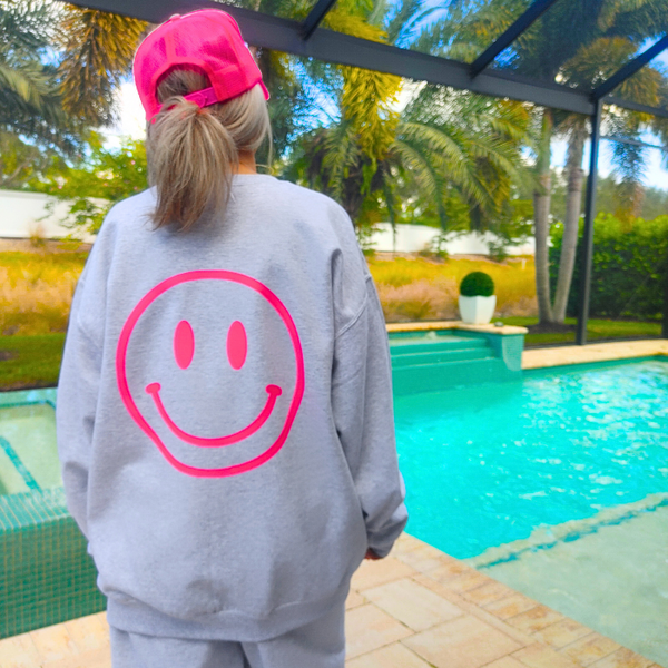 Bring all the good vibes with this cozy “Happy Is the New Rich” smiley face sweatshirt. Featuring a bold neon-pink front chest quote and an oversized happy face graphic on the back, this crewneck is designed to make every outfit feel a little brighter. This soft, comfy unisex crewneck makes the perfect gift and for everyday wear, this is your new go-to layer for errands, lounging, weekend adventures, and everything in between. Pair it with our matching sweatpants (sold separately) for the full set. 