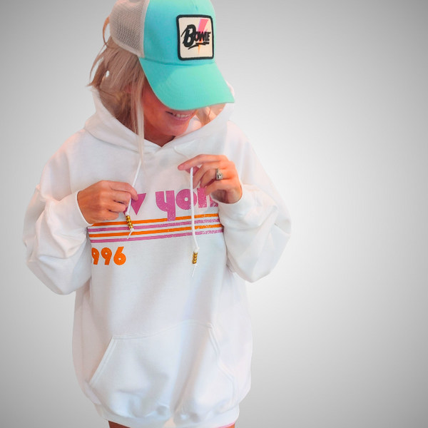 This New York Hoodie is the perfect blend of retro style and everyday comfort. Featuring a distressed New York graphic with vibrant pink and orange stripes, metallic gold beaded drawstrings, and a cozy unisex fit, it's a statement hoodie made for city lovers, travelers, and anyone who loves a bold vintage-inspired aesthetic. Size up 1–2 sizes for a cozy oversized look.