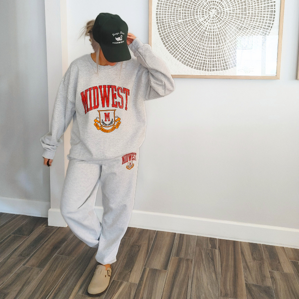 This Midwest Sweatshirt and Sweatpants Set combines cozy comfort with classic collegiate style. Featuring a distressed varsity-inspired Midwest graphic on a matching ash gray crewneck and jogger set, this outfit is perfect for travel days, casual weekends, running errands, or relaxing in ultimate comfort. Sweatpants feature a relaxed oversized fit, and for an oversized fit size up in our crewneck. Matching Midwest graphic t-shirt sold separately.