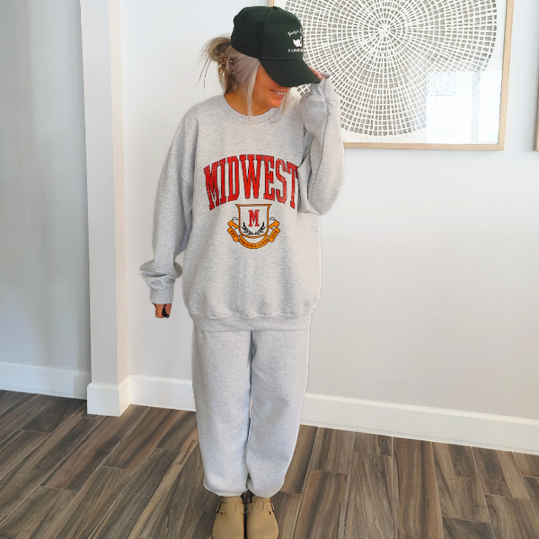 This Midwest Sweatshirt and Sweatpants Set combines cozy comfort with classic collegiate style. Featuring a distressed varsity-inspired Midwest graphic on a matching ash gray crewneck and jogger set, this outfit is perfect for travel days, casual weekends, running errands, or relaxing in ultimate comfort. Sweatpants feature a relaxed oversized fit, and for an oversized fit size up in our crewneck. Matching Midwest graphic t-shirt sold separately.
