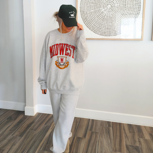 This Midwest Sweatshirt and Sweatpants Set combines cozy comfort with classic collegiate style. Featuring a distressed varsity-inspired Midwest graphic on a matching ash gray crewneck and jogger set, this outfit is perfect for travel days, casual weekends, running errands, or relaxing in ultimate comfort. Sweatpants feature a relaxed oversized fit, and for an oversized fit size up in our crewneck. Matching Midwest graphic t-shirt sold separately.