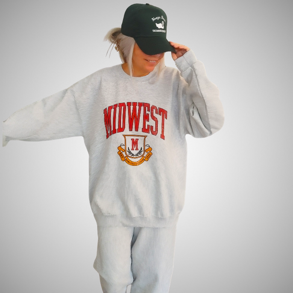 This Midwest Sweatshirt is the perfect blend of cozy comfort and classic collegiate style. Featuring a distressed varsity-inspired graphic on a soft ash gray crewneck, this unisex sweatshirt delivers an effortless retro look that's perfect for everyday wear, game days, travel, or lounging in comfort. Size up for an oversized sweatshirt look.