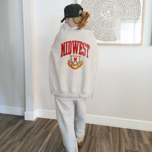 This Midwest Sweatshirt is the perfect blend of cozy comfort and classic collegiate style. Featuring a distressed varsity-inspired graphic on a soft ash gray crewneck, this unisex sweatshirt delivers an effortless retro look that's perfect for everyday wear, game days, travel, or lounging in comfort. Size up for an oversized sweatshirt look.